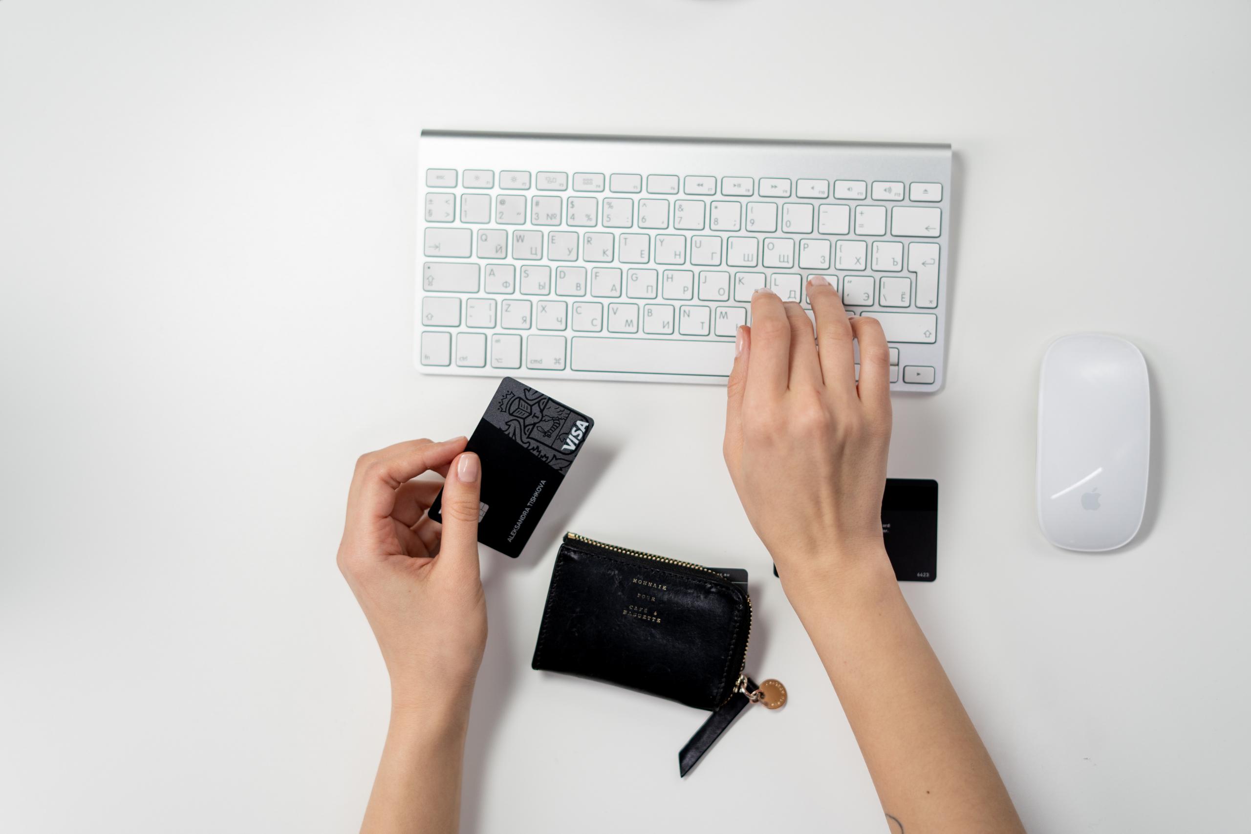 hand typing on a white keyboard while holding a black visa card